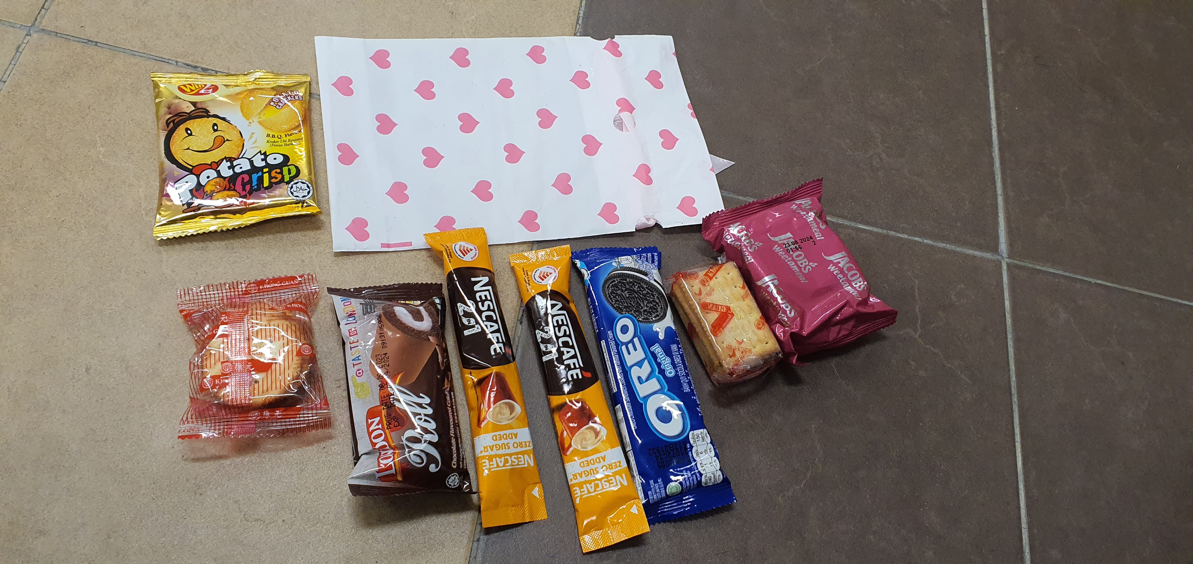Snacks including Oreo, Nescafe sticks, Potato Crisp, Jacobs crackers, and a chocolate roll on a tiled floor.