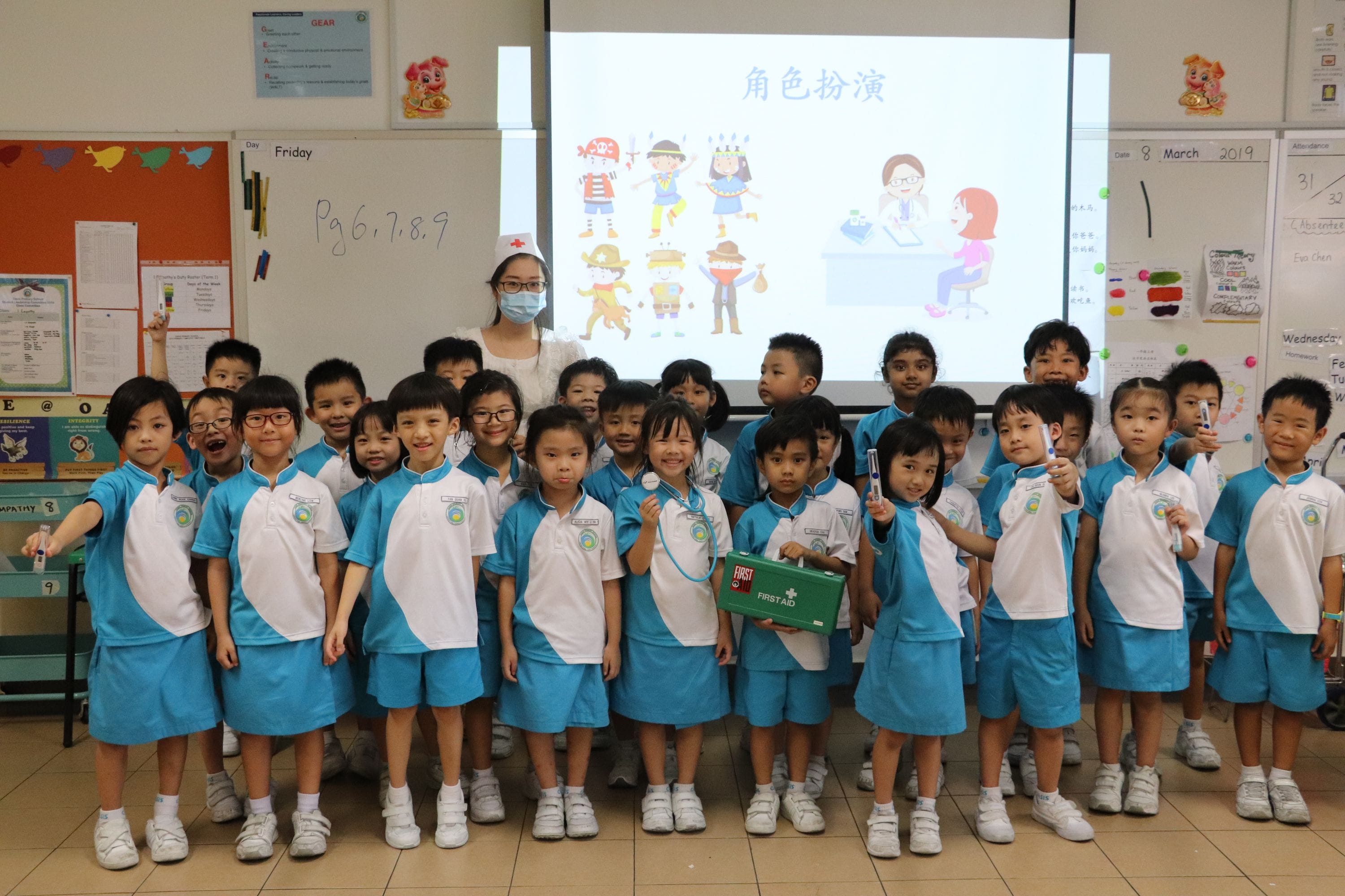 Young students in blue and white uniforms pose with a teacher in front of a Chinese-language classroom projector screen.
