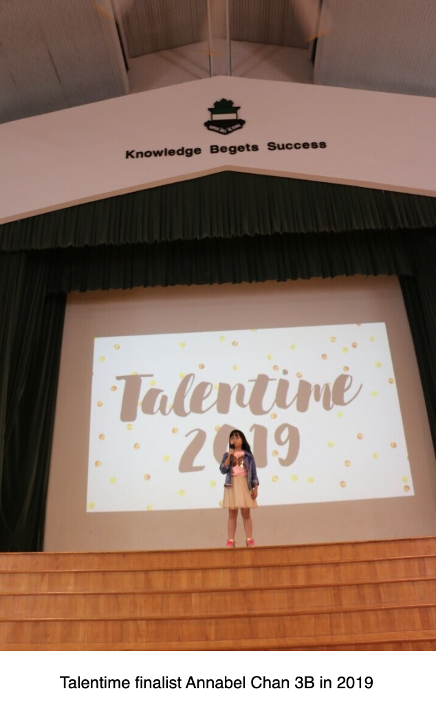 A young girl stands on a school stage in front of a projected "Talentime 2019" screen during a talent show.