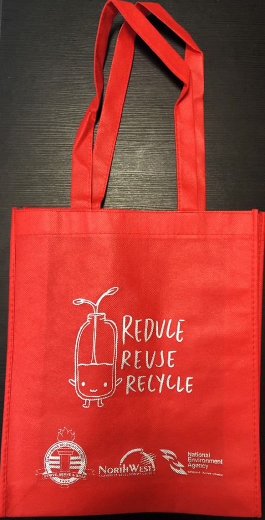 Red reusable tote bag printed with "Reduce Reuse Recycle" and a cute jar cartoon, with organization logos at the bottom.
