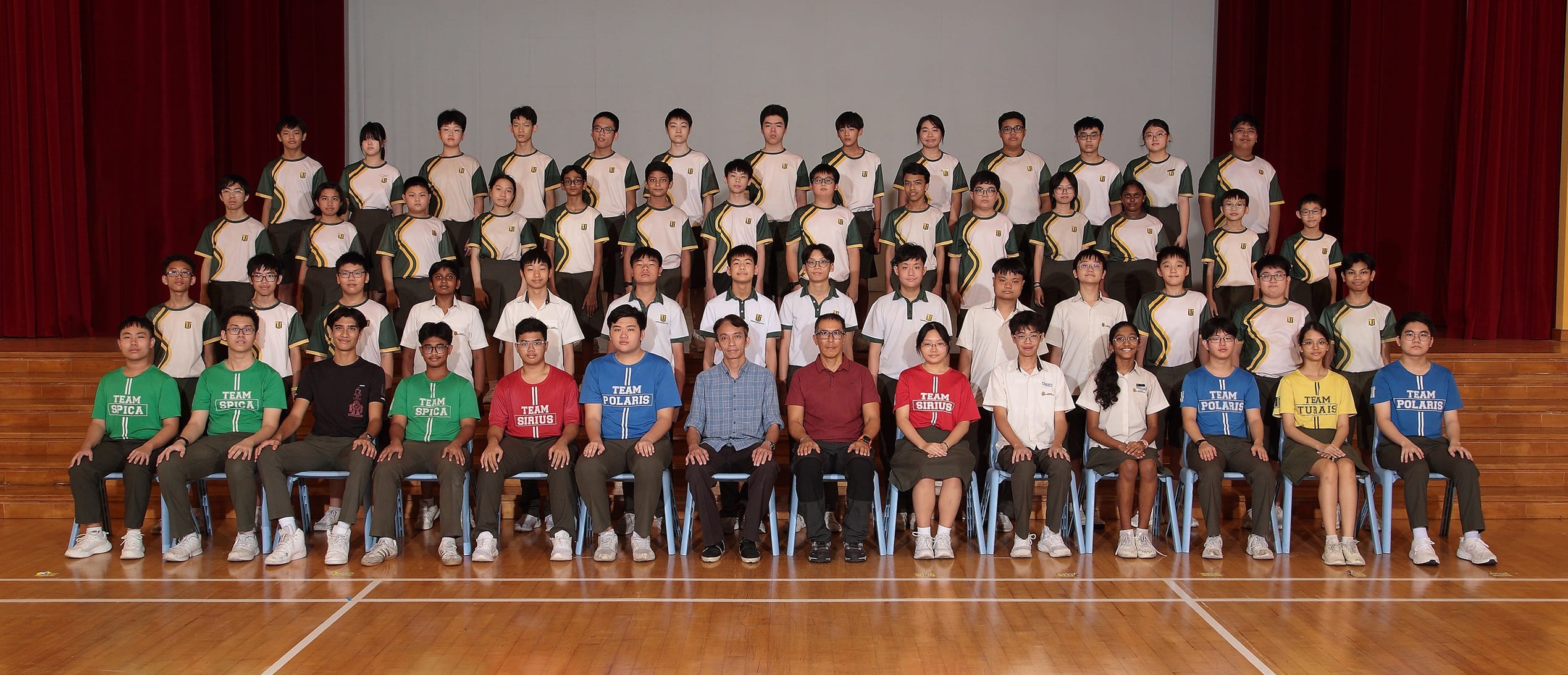 Large group of students in school uniforms and team t-shirts posed in rows with two adult teachers seated in front.