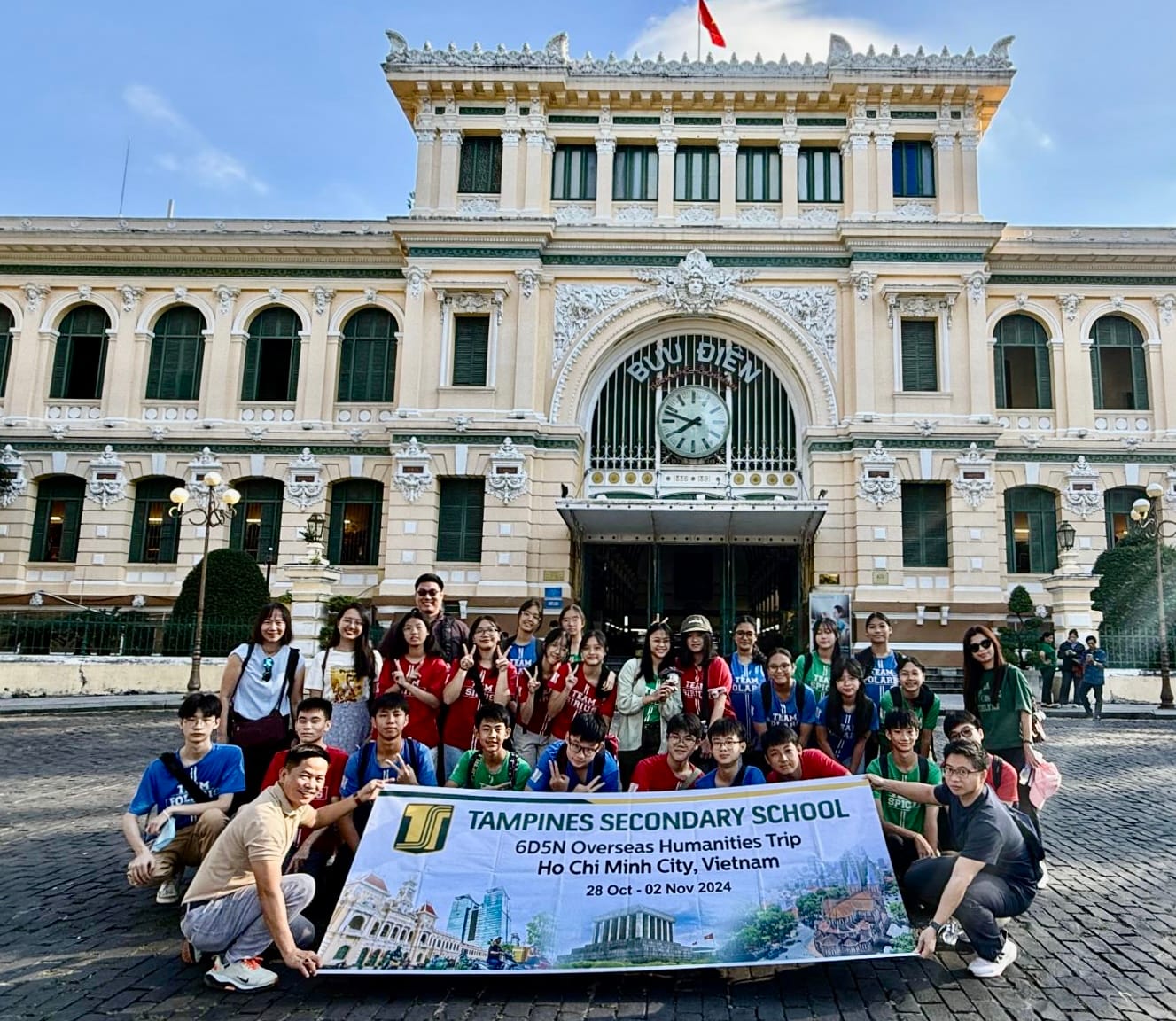 A student group holds a Tampines Secondary School banner in front of the Saigon Central Post Office in Vietnam.
