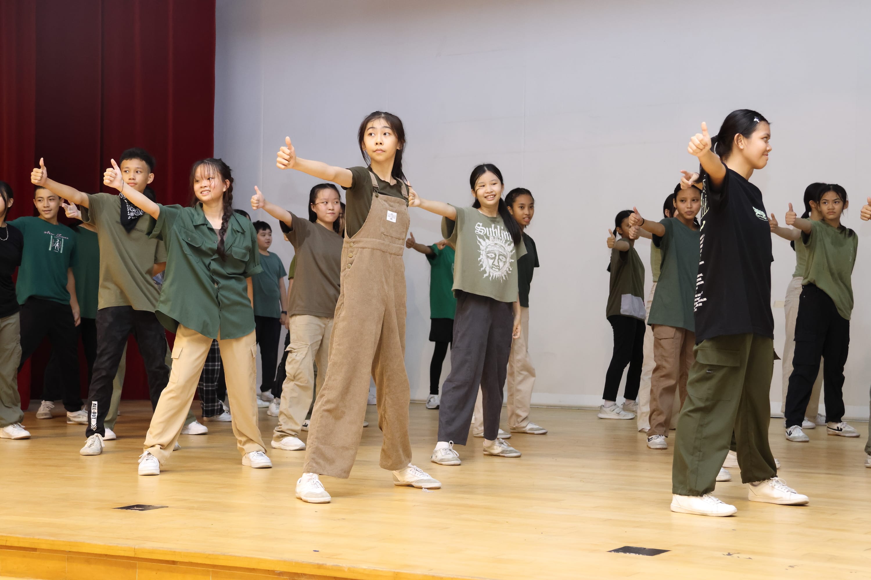 Group of teens on a stage with arms extended and thumbs up, practicing a dance routine.