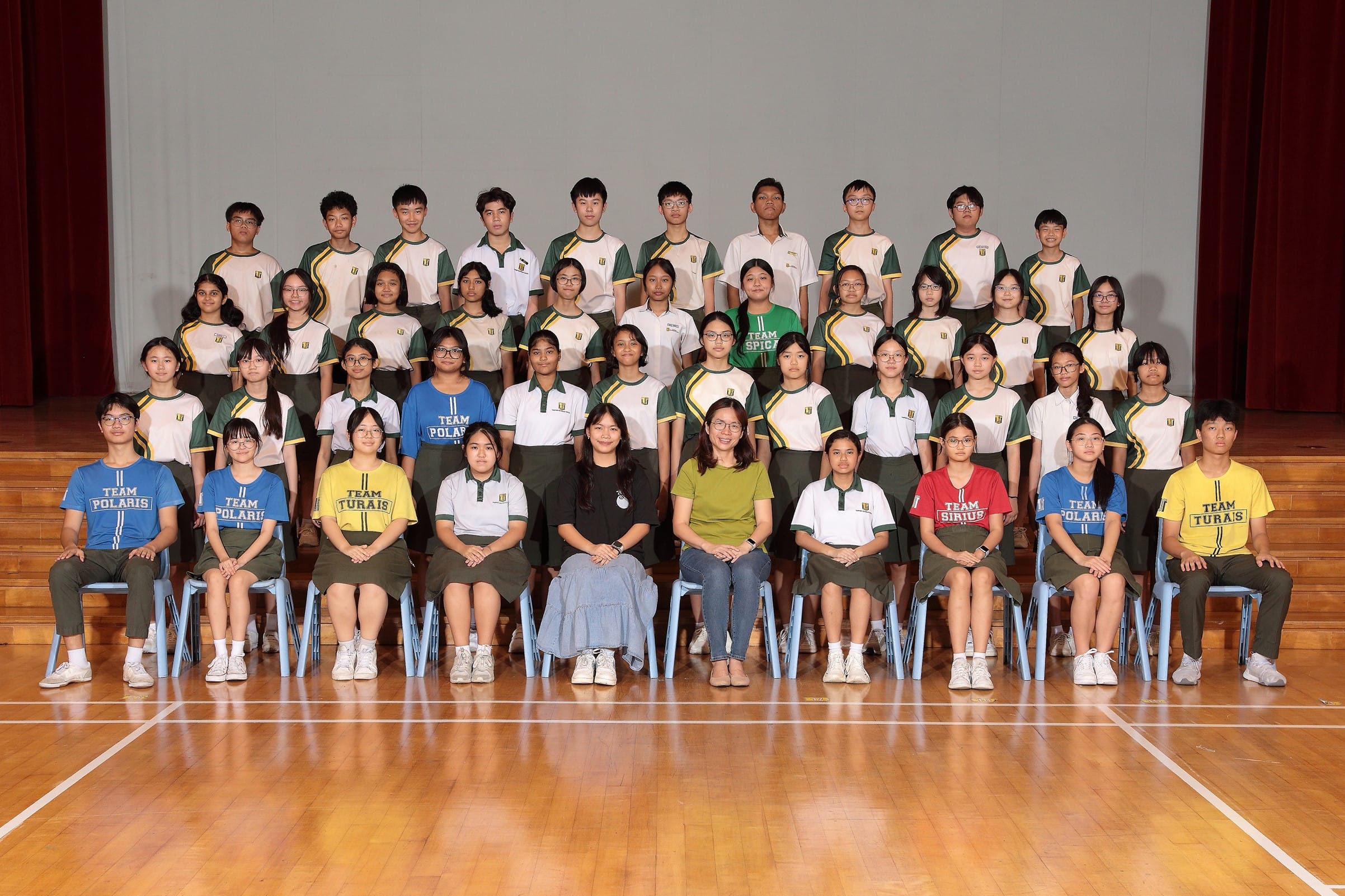 Large group of school students in green and white uniforms posing in rows with two teachers seated in front.