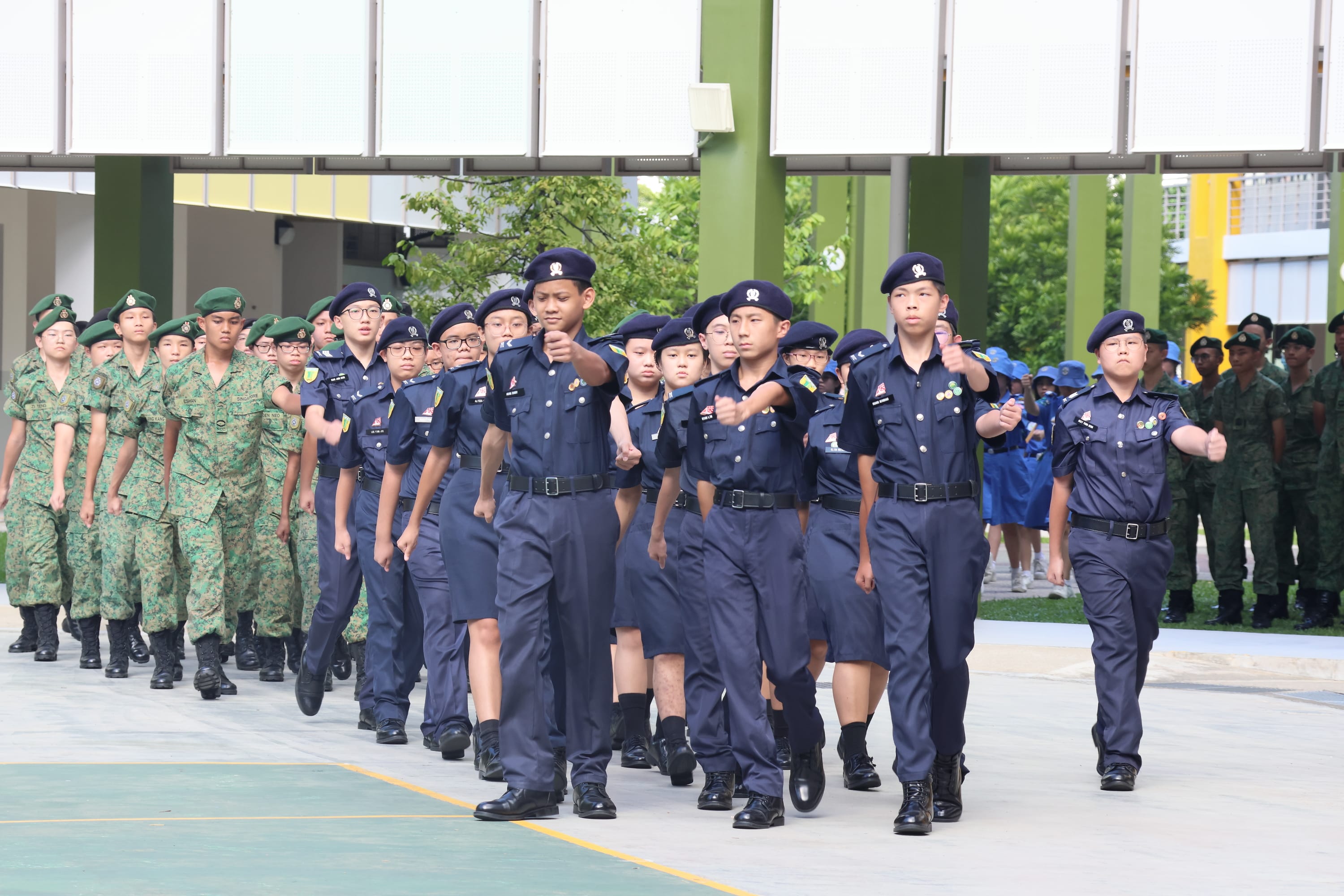 Uniformed cadets in navy march in formation, with others in green camouflage marching behind.