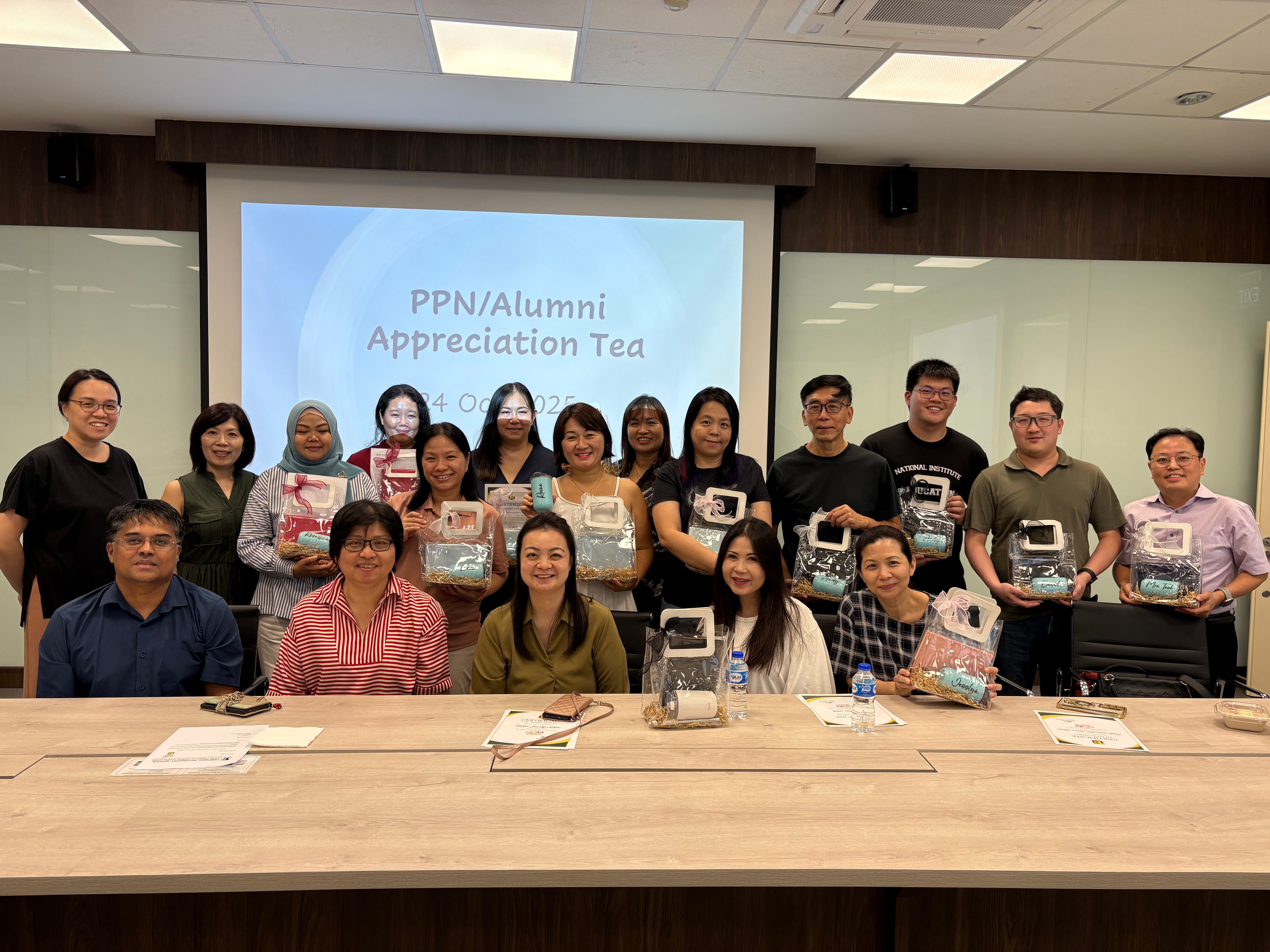Group photo in meeting room holding gift packs; projector screen reads PPN/Alumni Appreciation Tea.