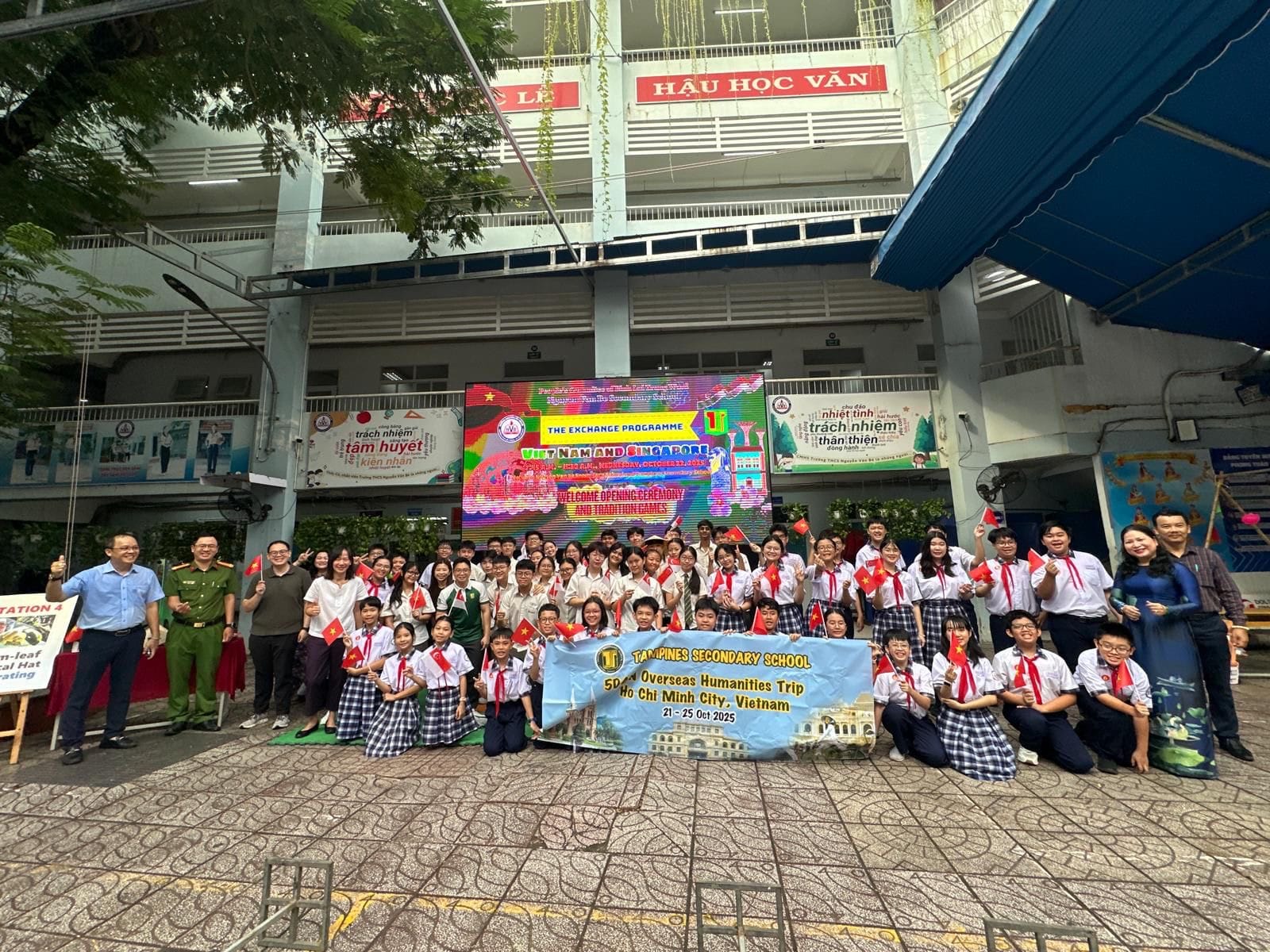 Large group of students and adults pose outdoors holding Vietnamese flags and a Tampines Secondary School banner in Ho Chi Minh City.