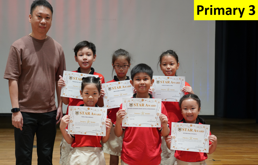 Six Primary 3 children in red uniforms hold Star Award certificates, standing with an adult male teacher on a stage.