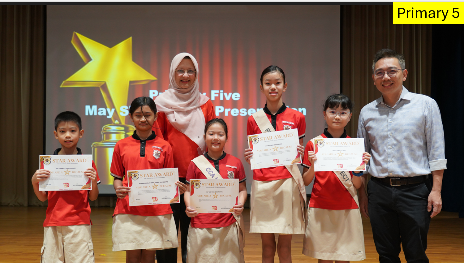 Five Primary 5 students hold Star Award certificates, flanked by two adults on a stage with a star trophy backdrop.
