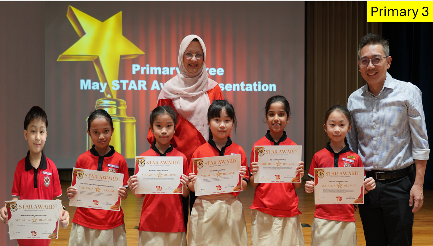 Six Primary 3 students hold Star Award certificates, flanked by two adult presenters on a stage.