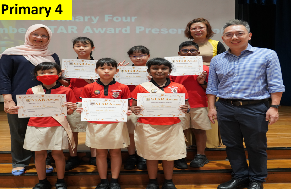 Primary 4 students in red uniforms hold STAR Award certificates, flanked by two adult teachers on a stage.