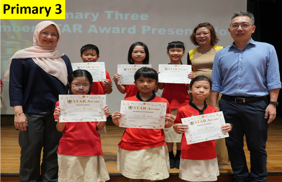 Six Primary 3 students in red uniforms hold Star Award certificates, flanked by two teachers on a stage.