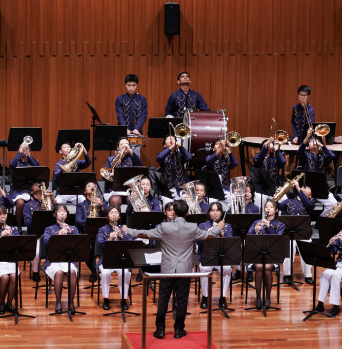 Students perform in a concert band on stage under the direction of a conductor.