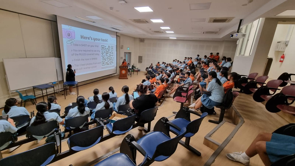 Add your alt text herePhotograph of a classroom lecture showing students seated and facing a presenter at a podium with a large projection screen displaying a slide titled "Here's your link!"