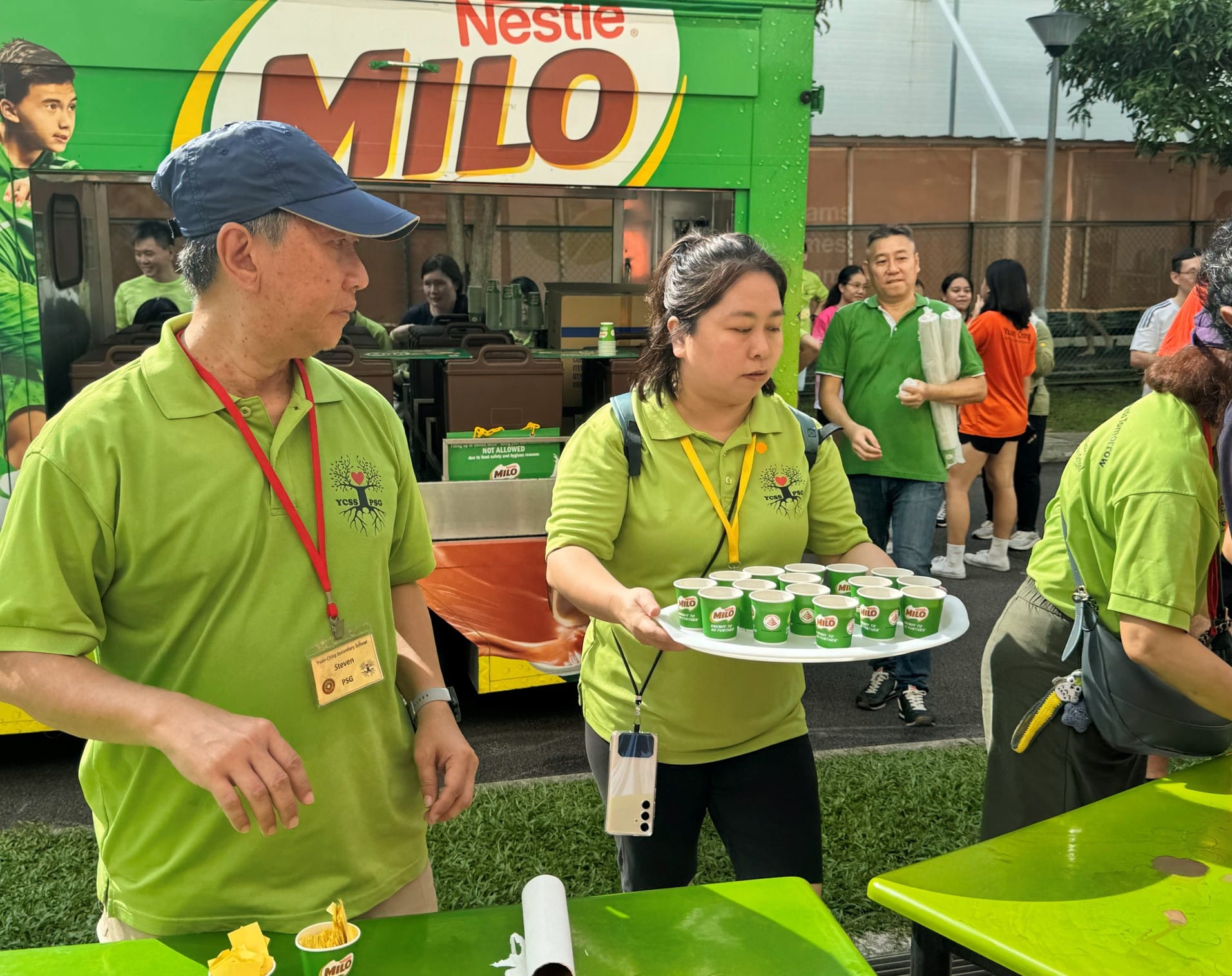 Woman in green shirt carries a tray of Milo cups near a Nestle Milo truck at an outdoor event.