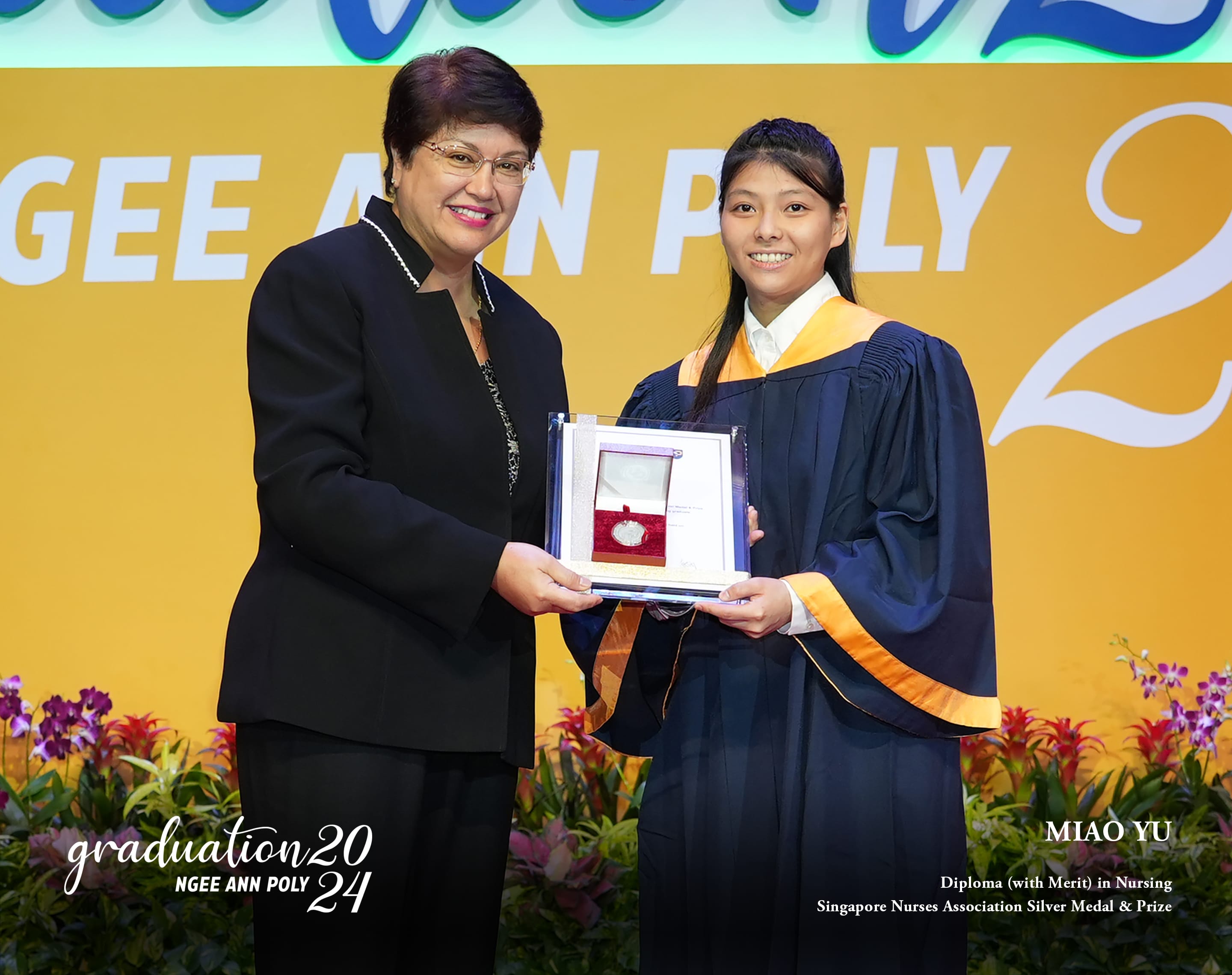 Two women hold a medal award at Ngee Ann Poly 2024 graduation, one in academic gown with gold sash.