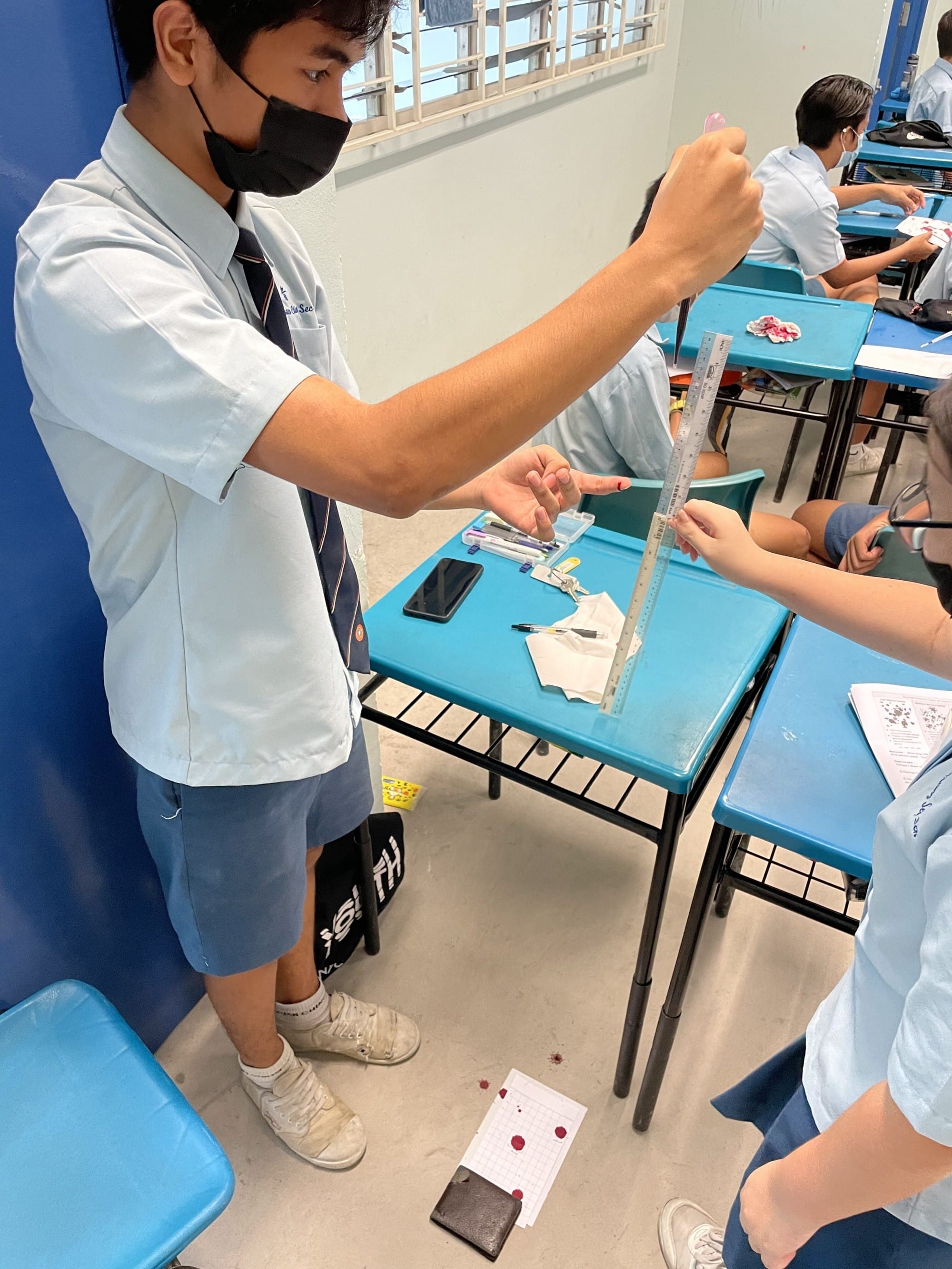 Student uses a dropper and ruler to measure liquid during a hands-on science experiment while classmates observe at nearby desks.