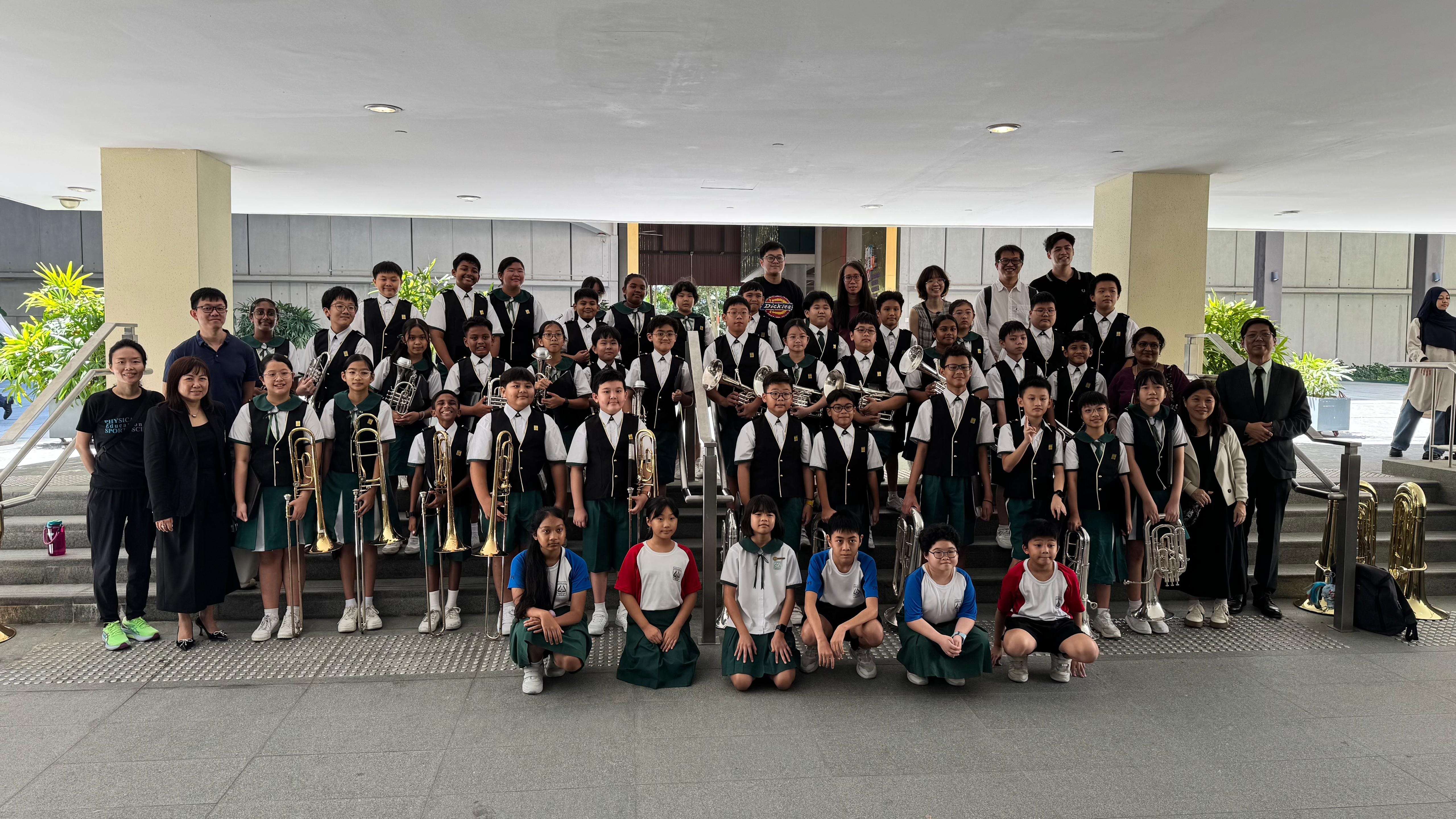 Large group of school students in uniforms posing on steps with brass instruments including trombones and trumpets.