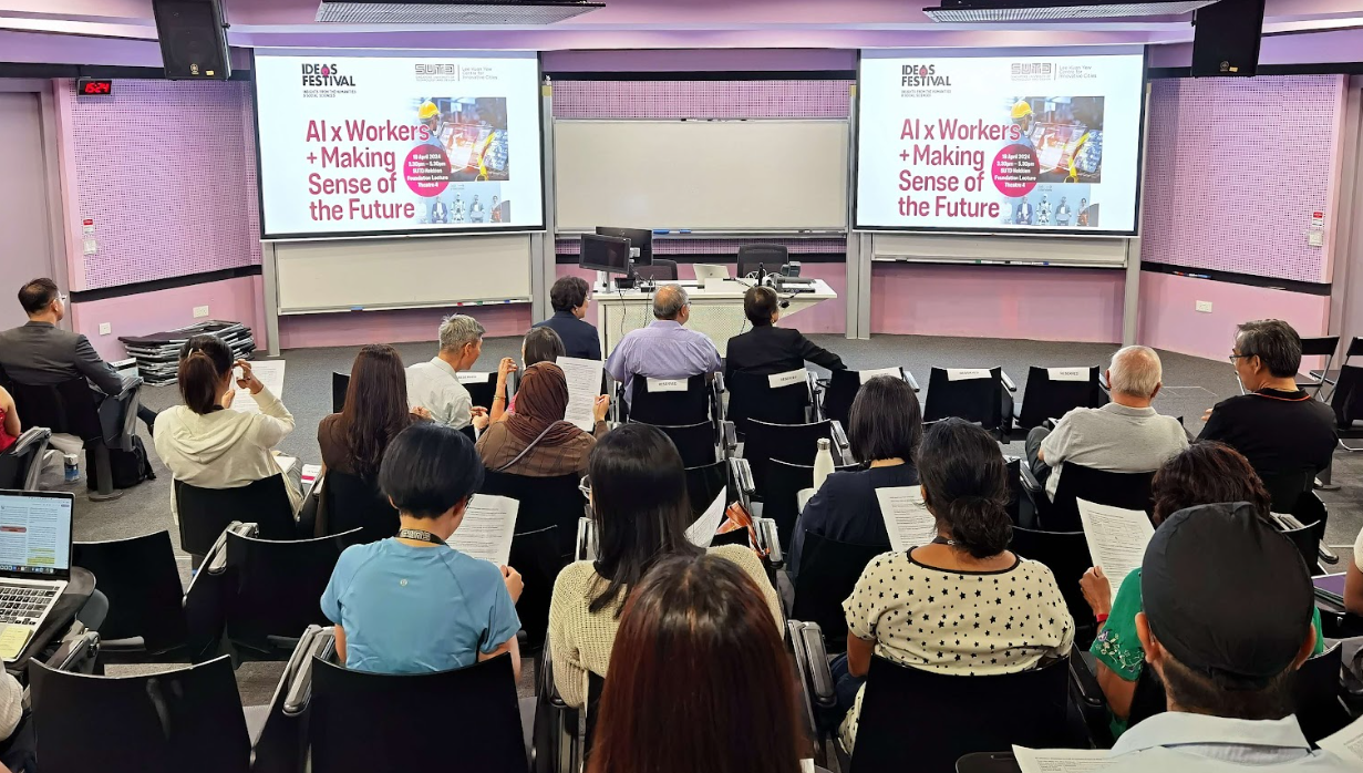 Audience seated in a lecture hall facing two screens displaying "AI x Workers + Making Sense of the Future" at an Ideas Festival.