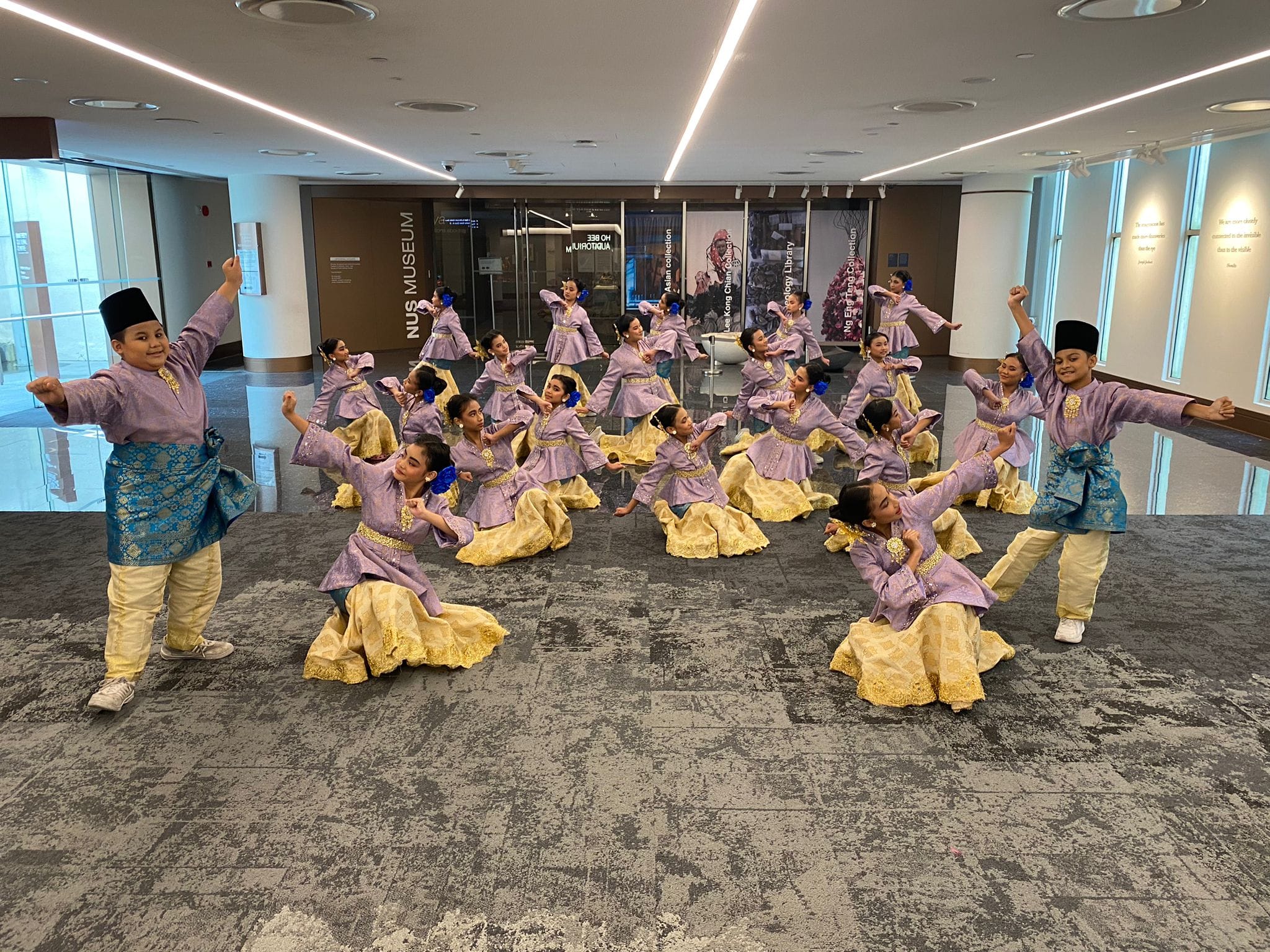 A group of children in purple and gold traditional Malay costumes perform a dance inside NUS Museum.