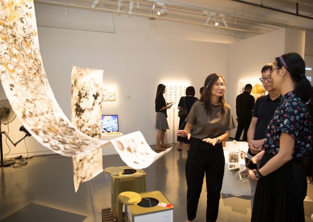 Three visitors examine a flowing patterned artwork in a modern gallery with white walls and track lighting.
