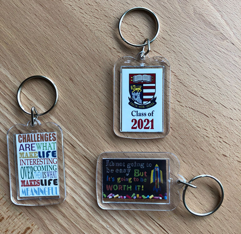 Three keychains on wood: motivational quotes and a school crest "Class of 2021" keychain.
