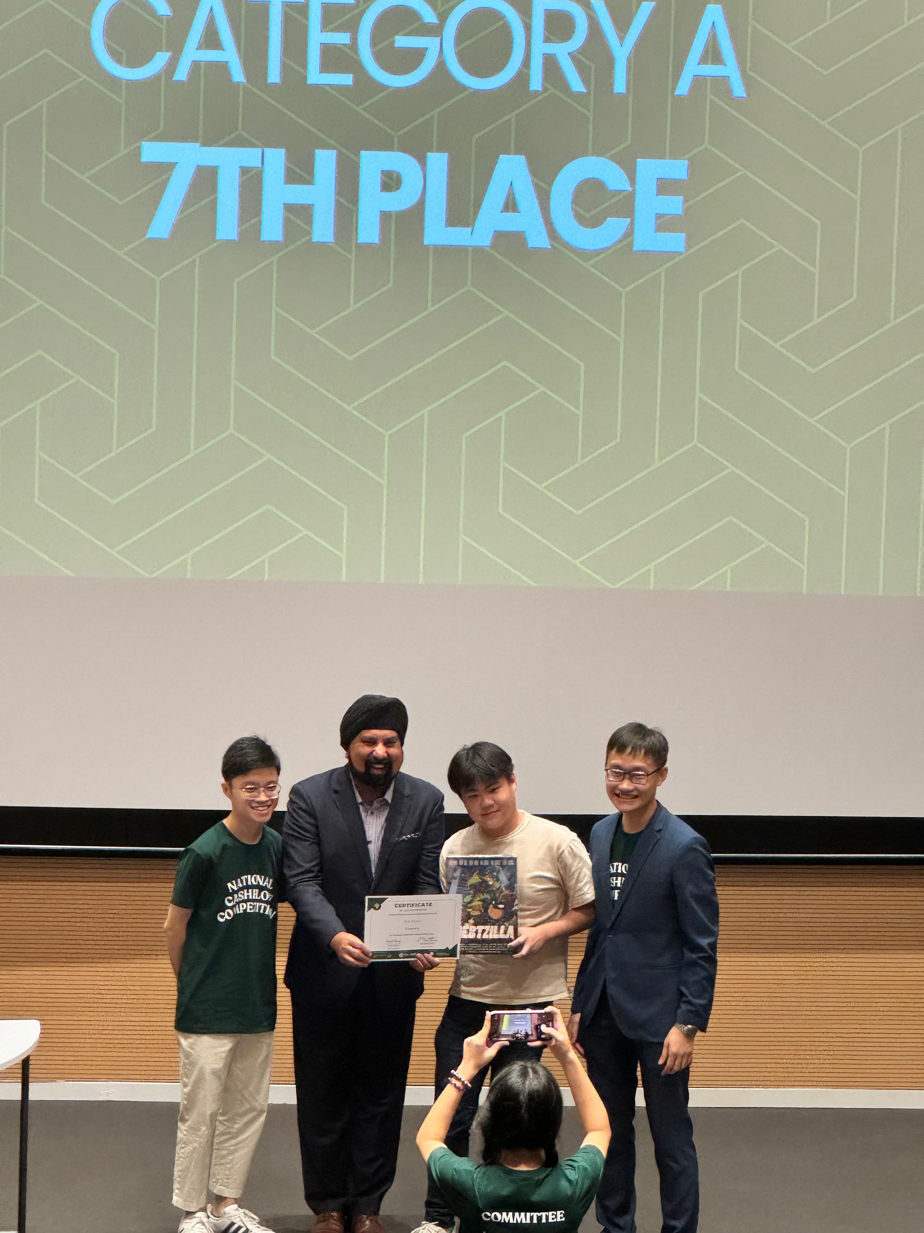 A student proudly receives a certificate of achievement and a prize on stage from a presenter alongside event organizers.