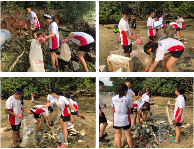 Students in white and red uniforms collect litter in large bags during a beach cleanup near a shoreline.