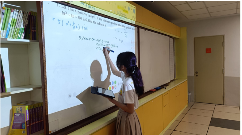 BDS student holding an iPad while working through a quadratic equation math problem on the classroom’s whiteboard.