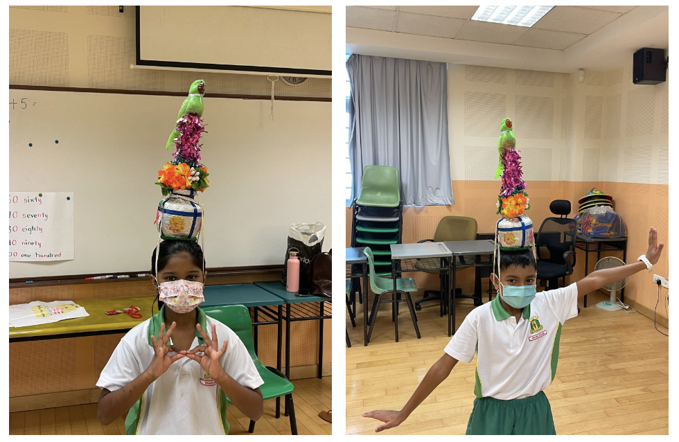 Two masked students in school uniforms balance colorful decorated pots topped with a green parrot on their heads.