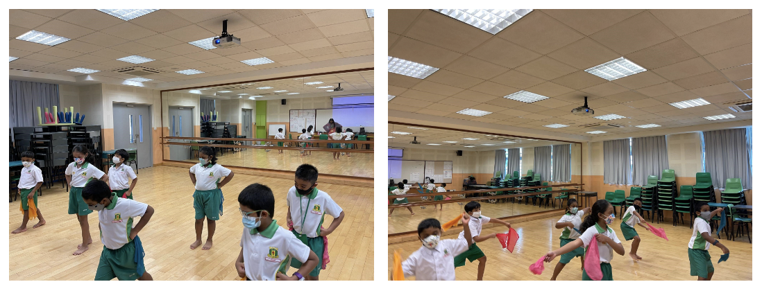 Children in school uniforms and masks dance with colorful scarves in a mirrored studio with wooden floors.