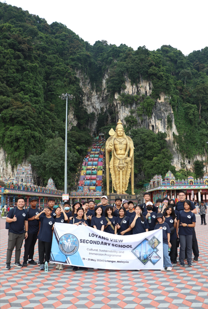 Group of students holding a Loyang View Secondary School banner at Batu Caves, Malaysia, with the golden Murugan statue behind them.