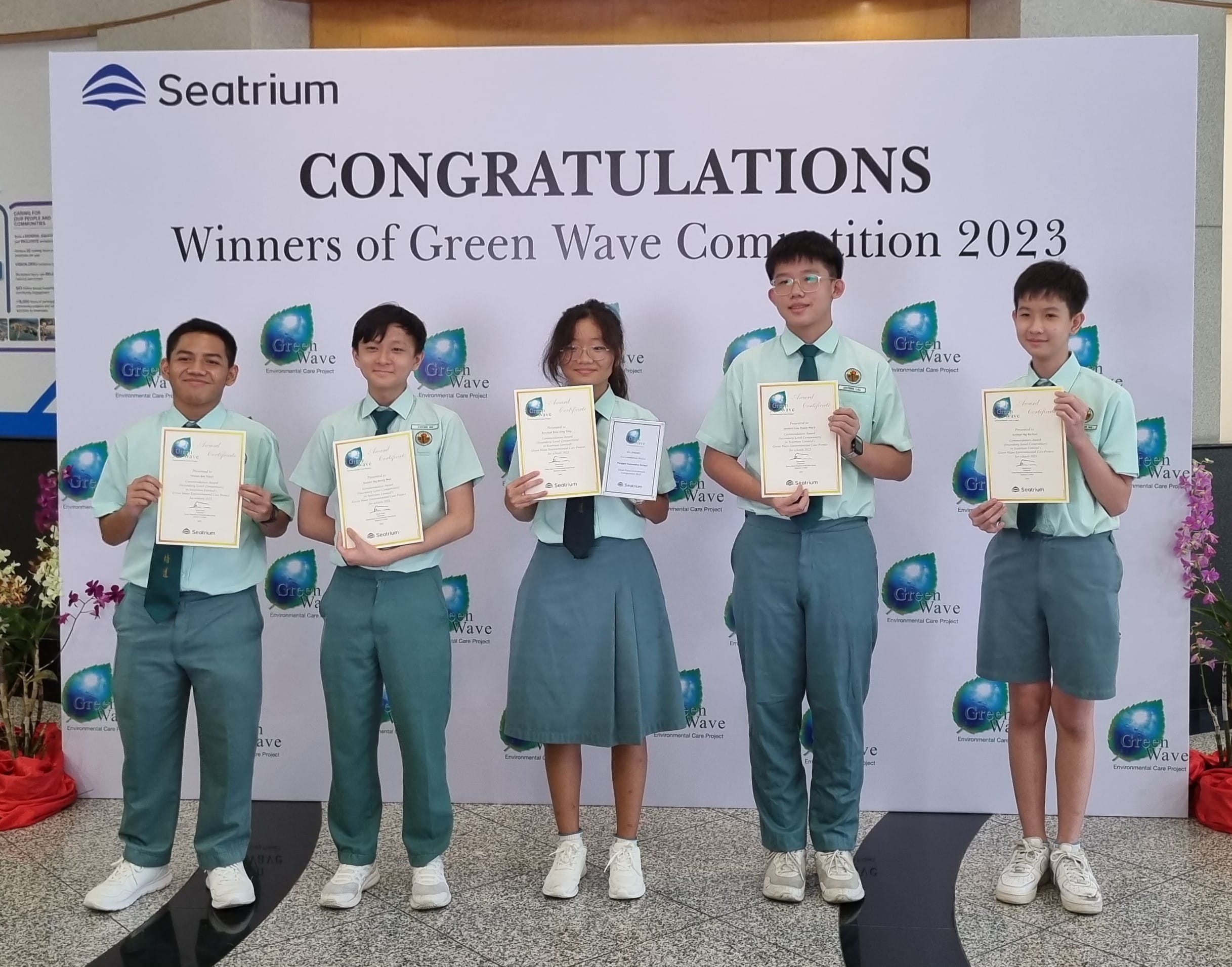 Five students in teal uniforms hold certificates in front of a Seatrium Green Wave Competition 2023 winners banner.