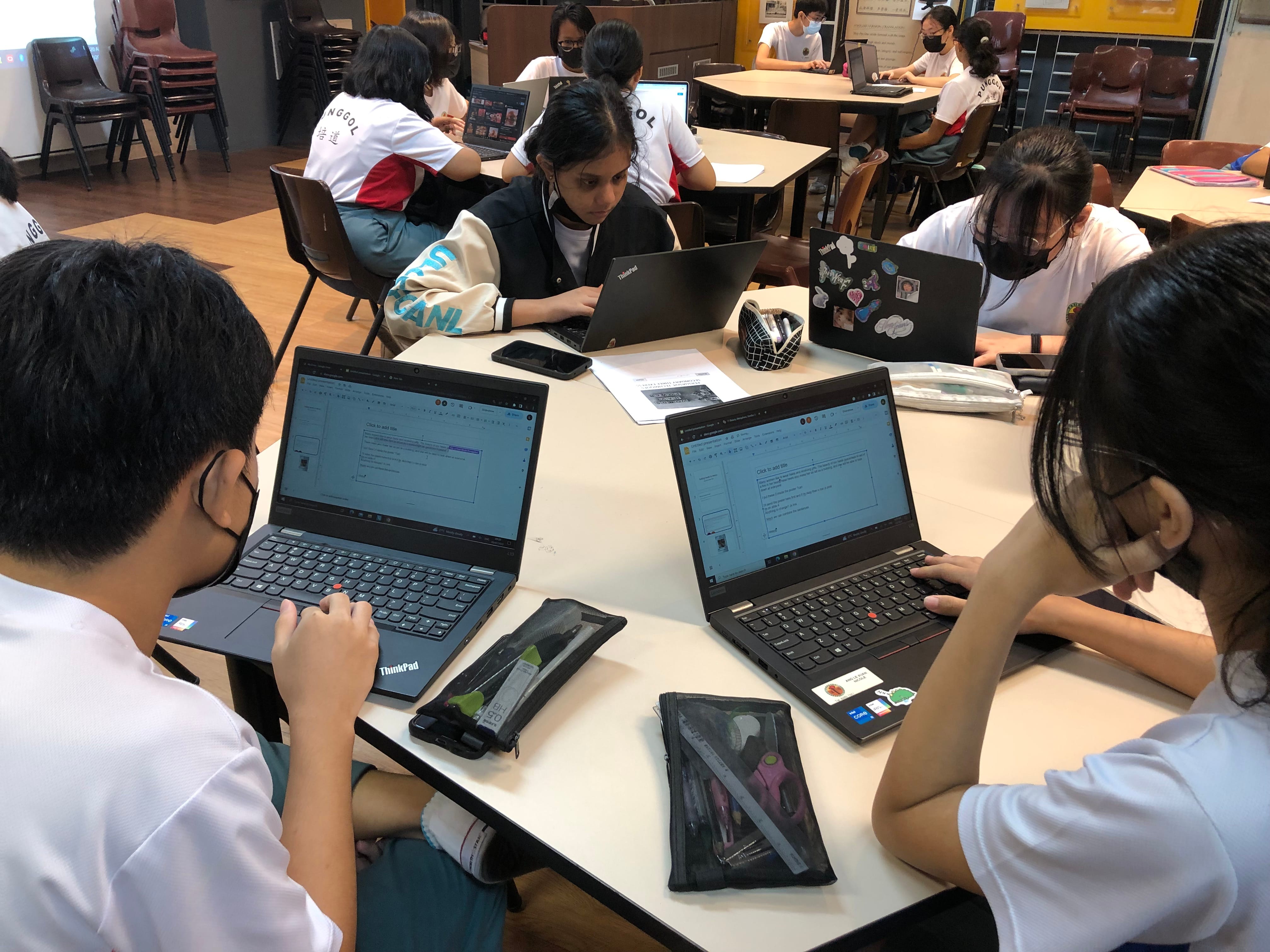 Students in school uniforms sit at tables working on ThinkPad laptops in a classroom setting.