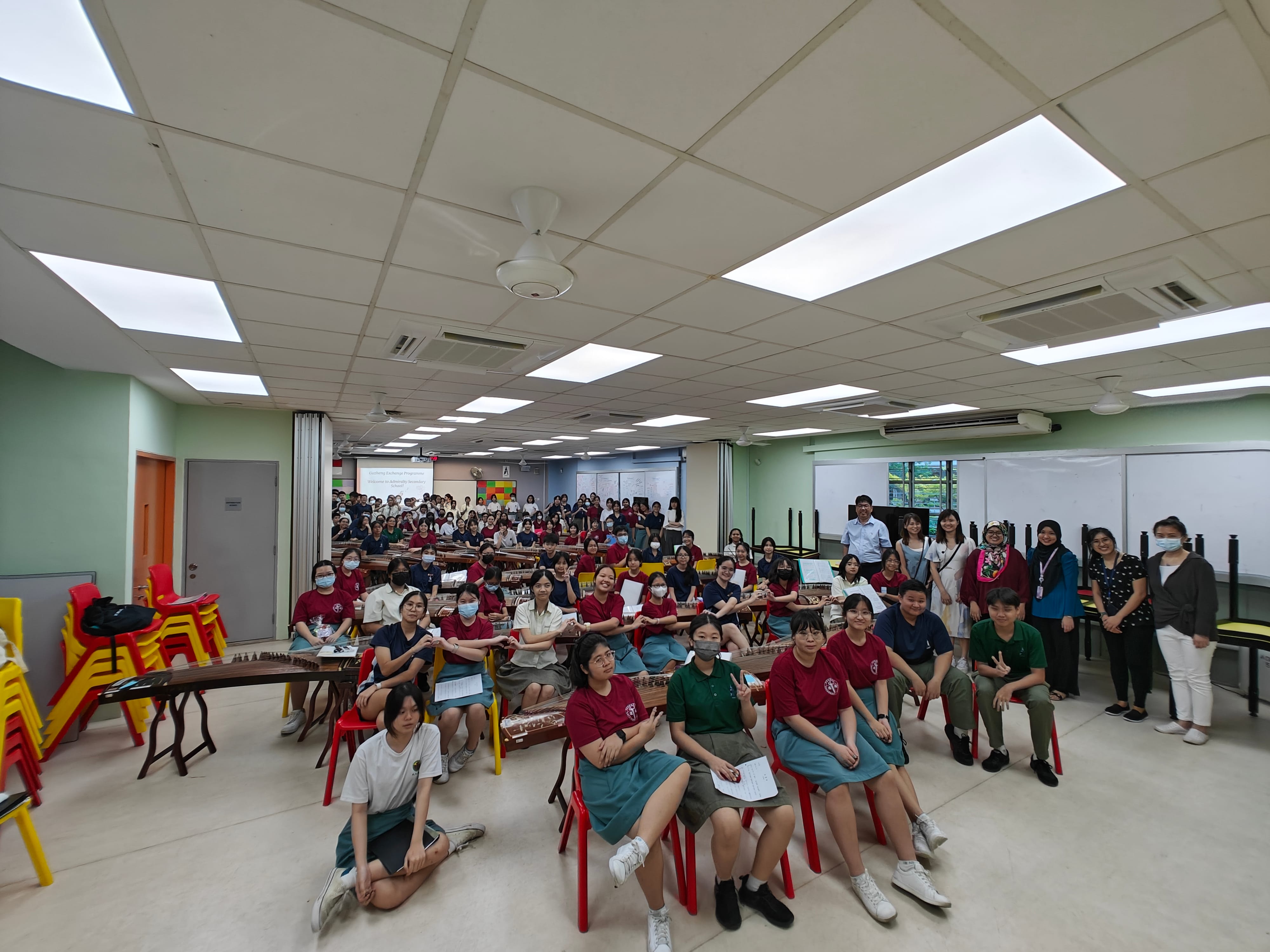 Large group of students in red uniforms seated in a bright classroom with traditional string instruments on tables.