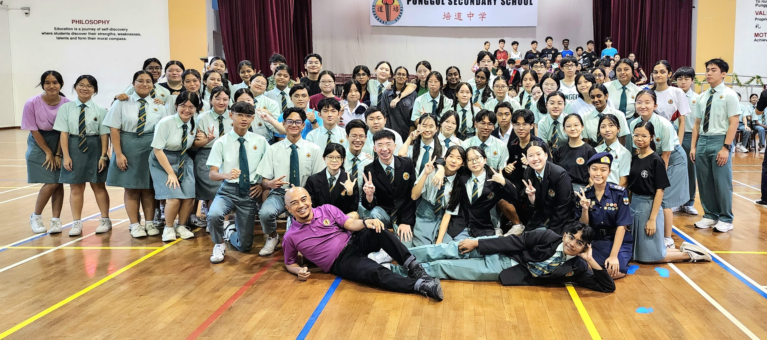 Large group of uniformed students and a teacher posing together in Punggol Secondary School hall.