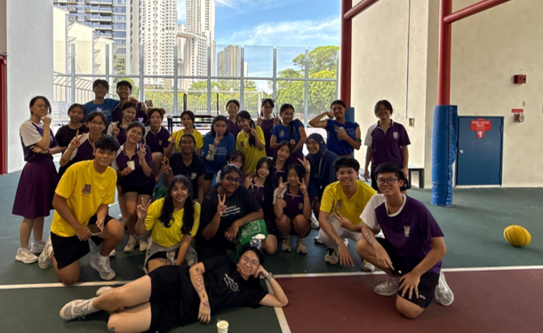 A large group of students in yellow and purple uniforms posing together on an indoor sports court.