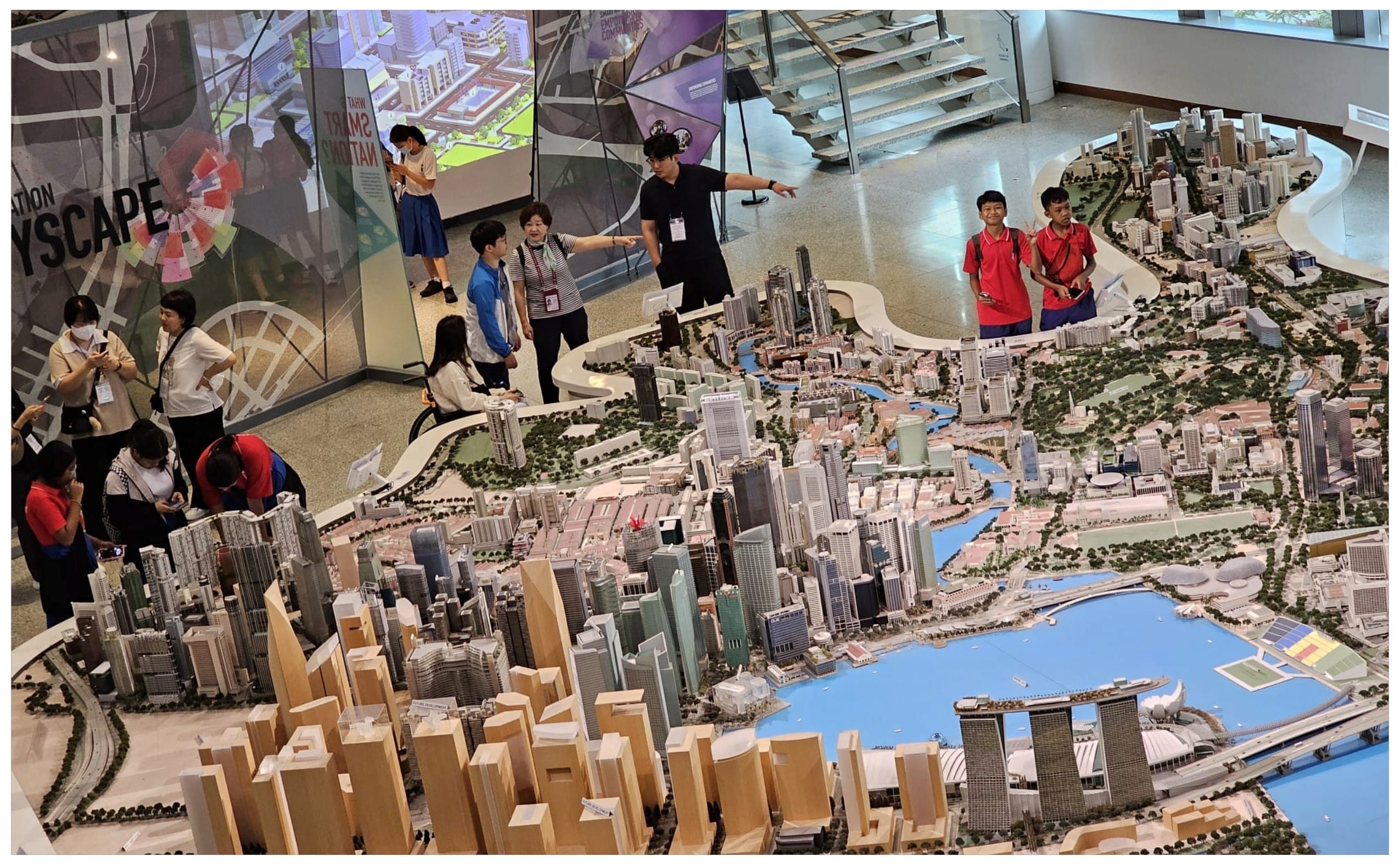Visitors stand around a large detailed scale model of Singapore's cityscape with buildings, waterways, and green spaces.