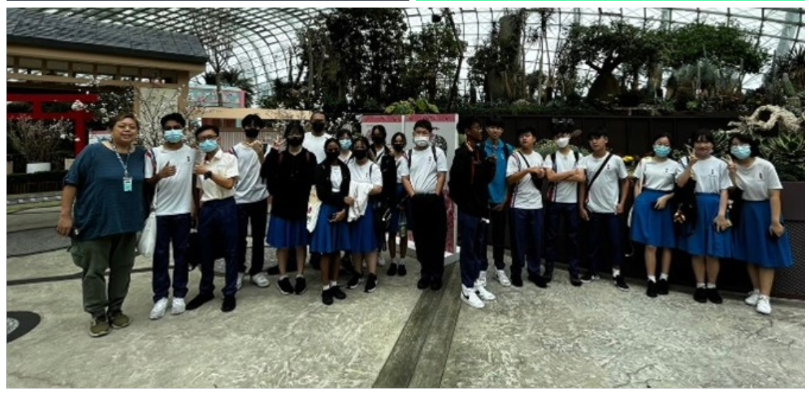 A group of masked students in school uniforms pose together inside a large glass dome greenhouse.