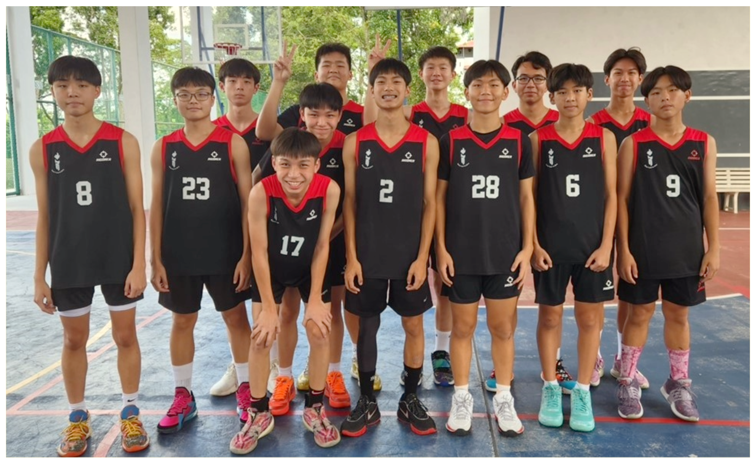 Group of teen boys in black-and-red basketball uniforms posing on an indoor court, one flashing peace signs.