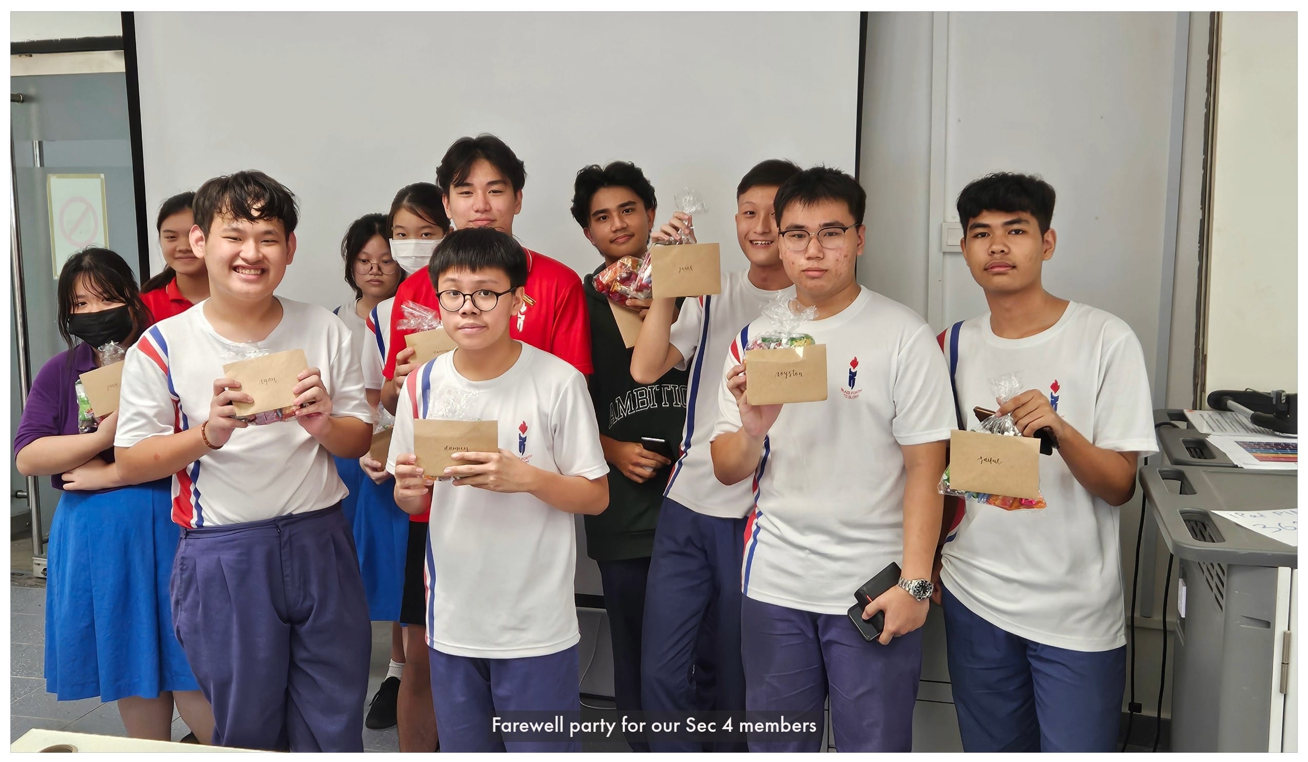 A group of students in school uniforms holding small kraft paper gift bags and candy packages indoors.