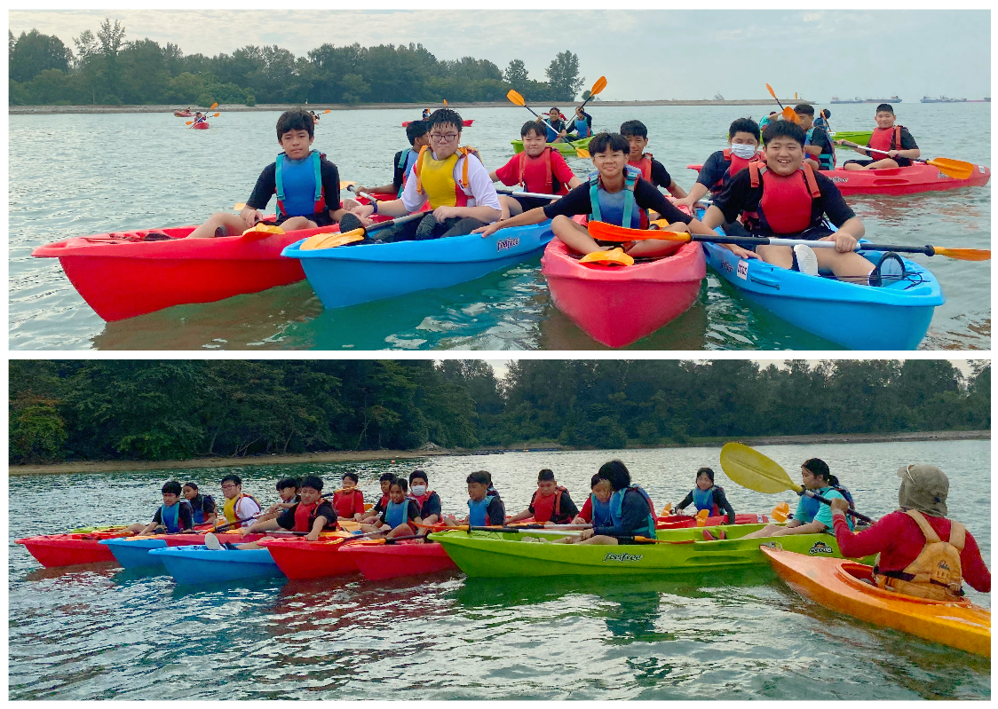 A group of young students wearing life jackets paddle colorful kayaks on calm water near a tree-lined shore.