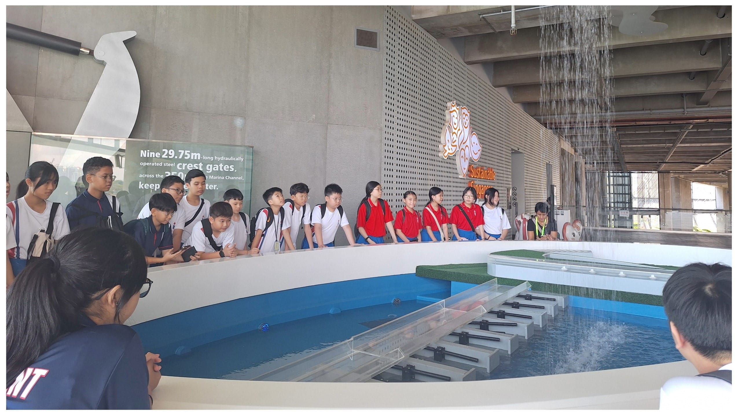 Students in school uniforms stand around a water gate scale model exhibit at the Sustainable Singapore Gallery.