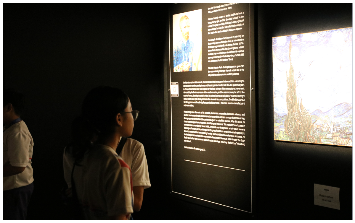 Two children read a dark museum panel about Van Gogh, with his self-portrait and a painting displayed nearby.