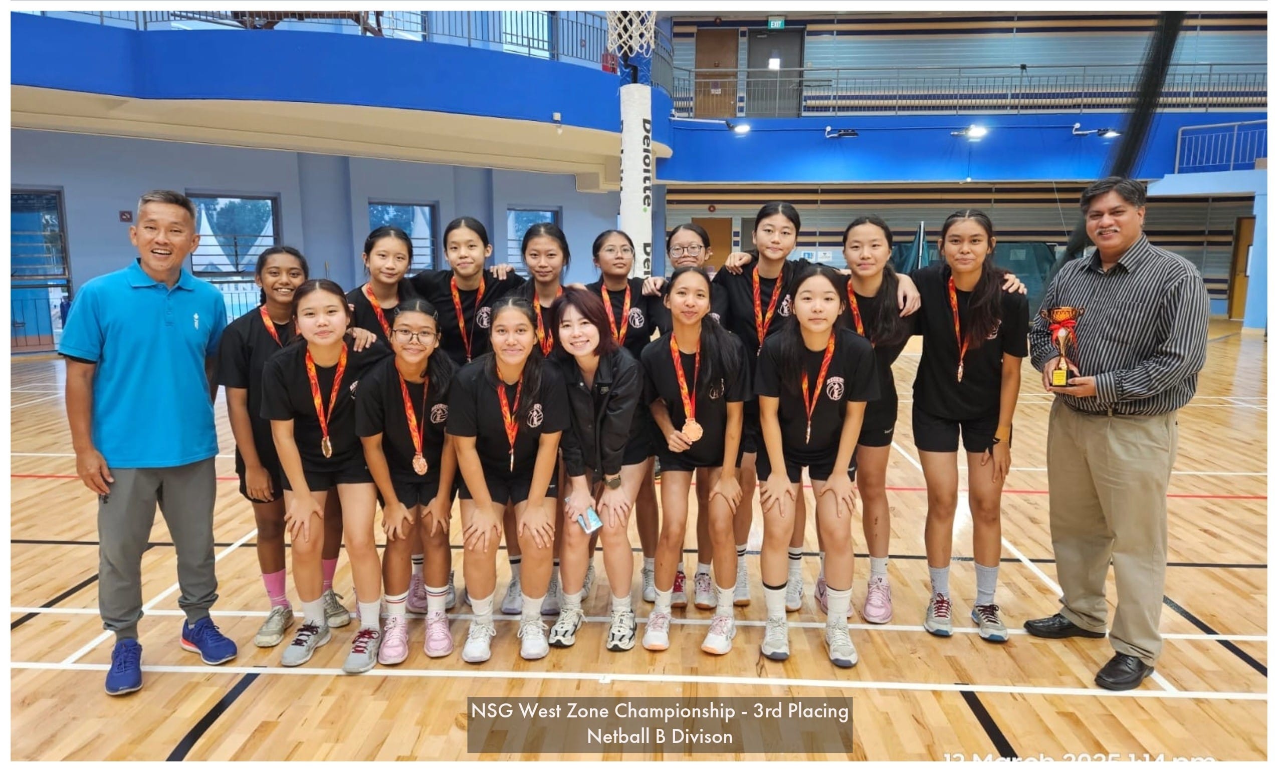 A netball team in black uniforms with medals poses indoors for NSG West Zone Championship 3rd place in Netball B Division.