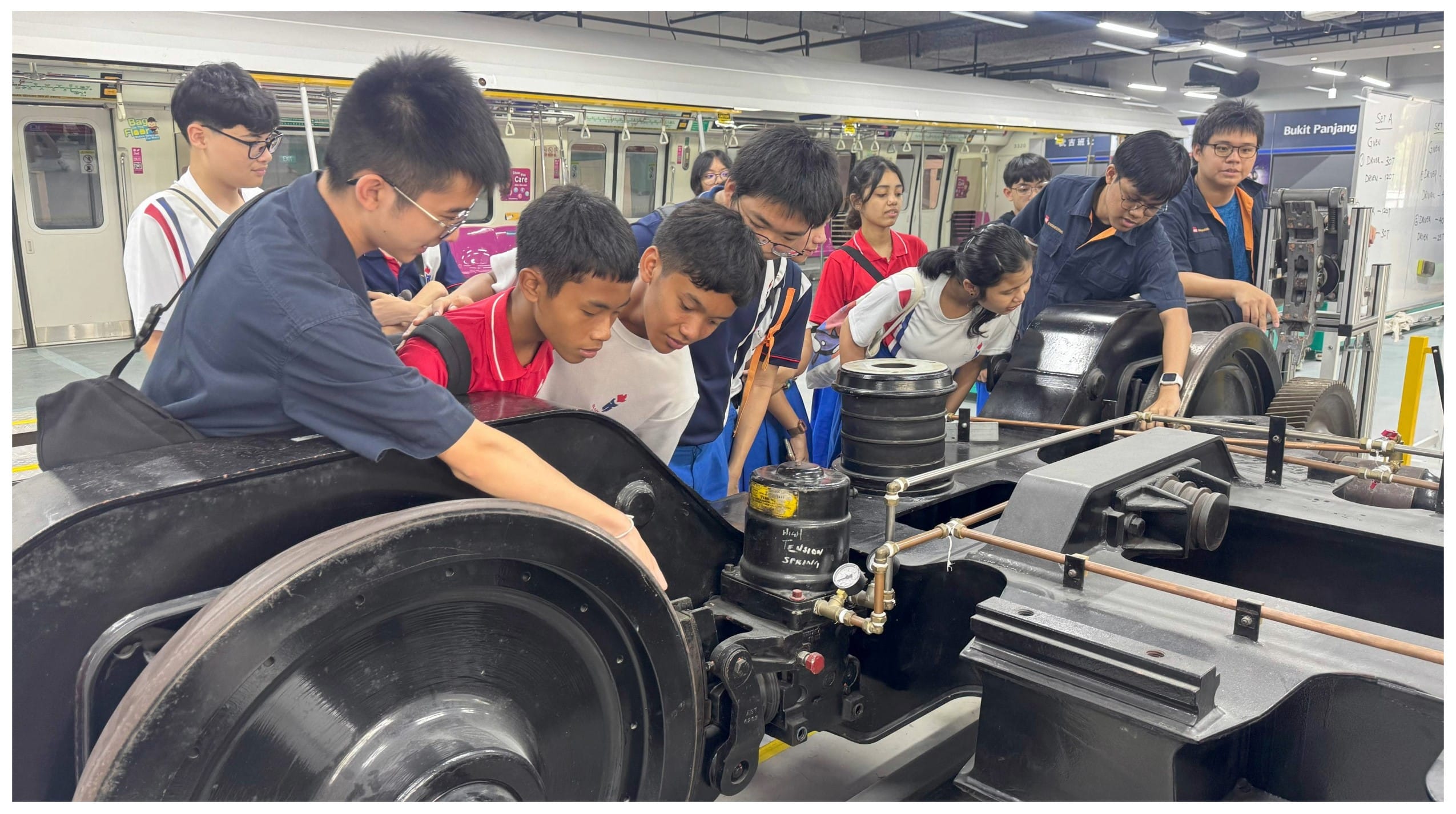 Students huddle around a train bogie mechanism at Bukit Panjang MRT station during an educational tour.