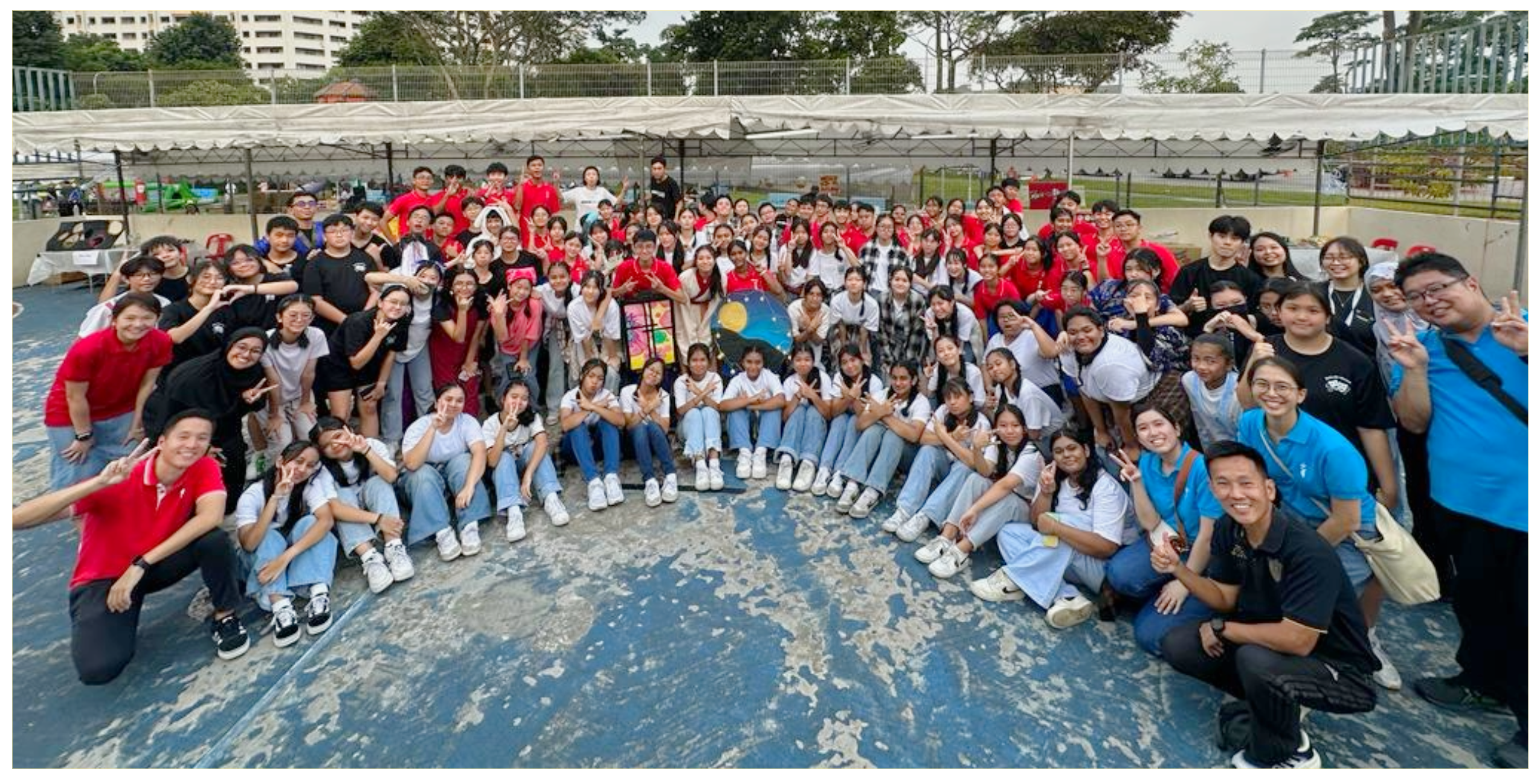 Large group of students and adults posing on a court under a canopy, many making peace signs.
