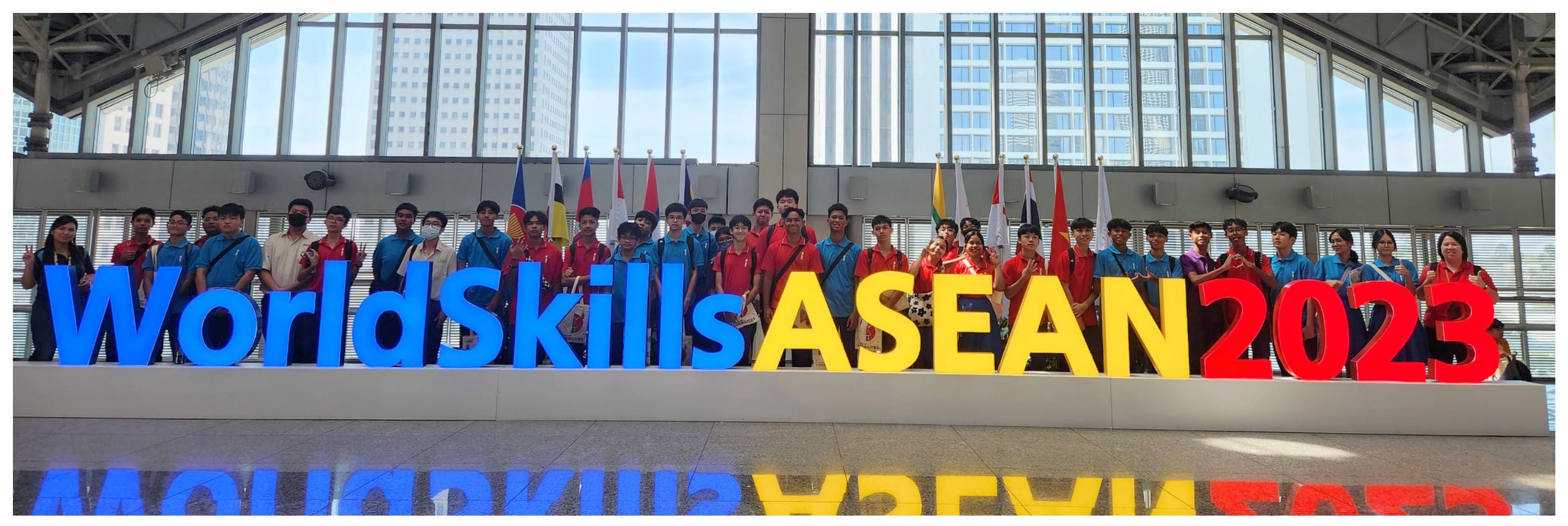 Group of young people posing behind large colorful WorldSkills ASEAN 2023 letters inside a convention hall.