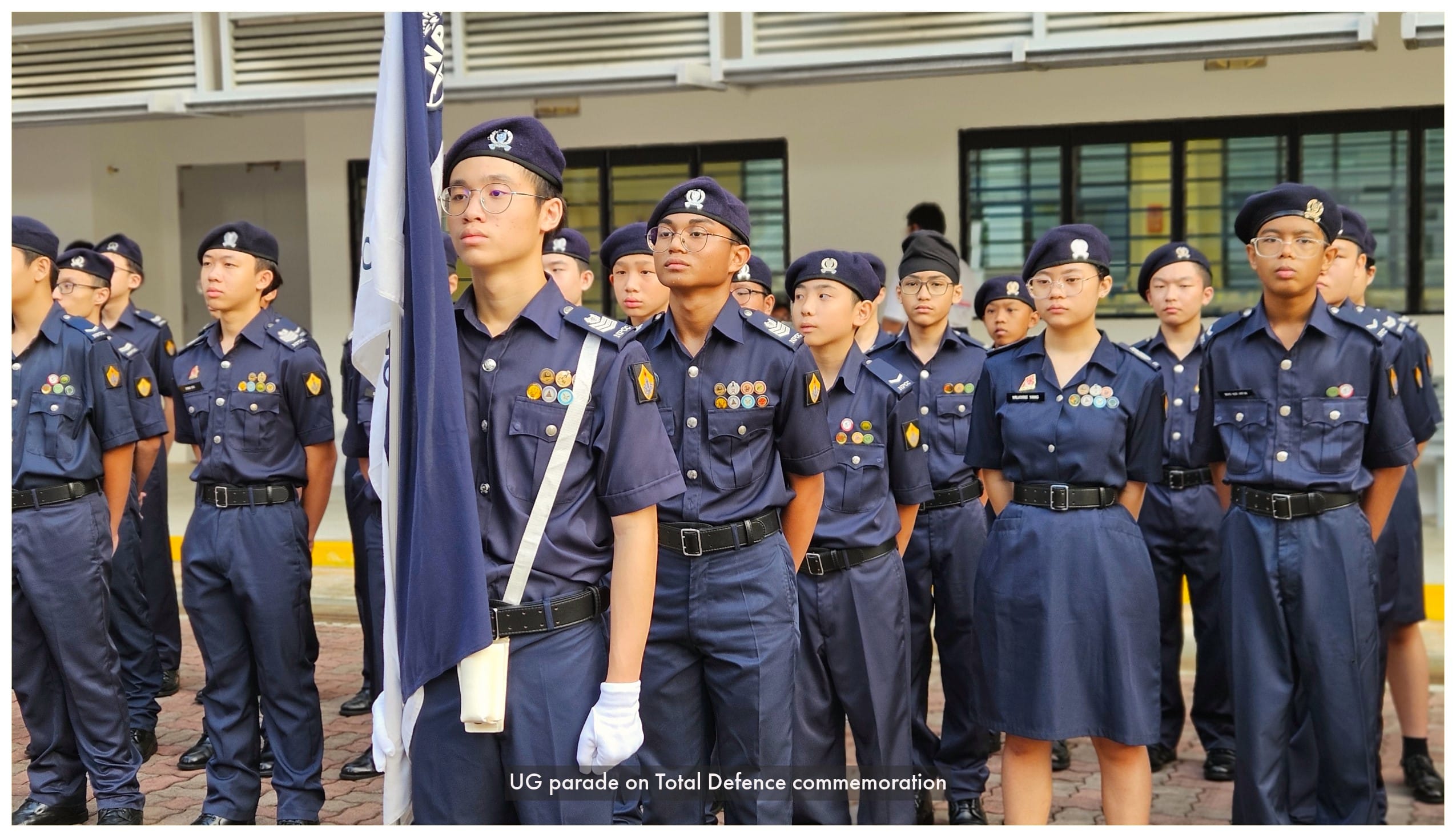 Young cadets in navy blue uniforms and berets stand at attention during a parade, one holding a flag.