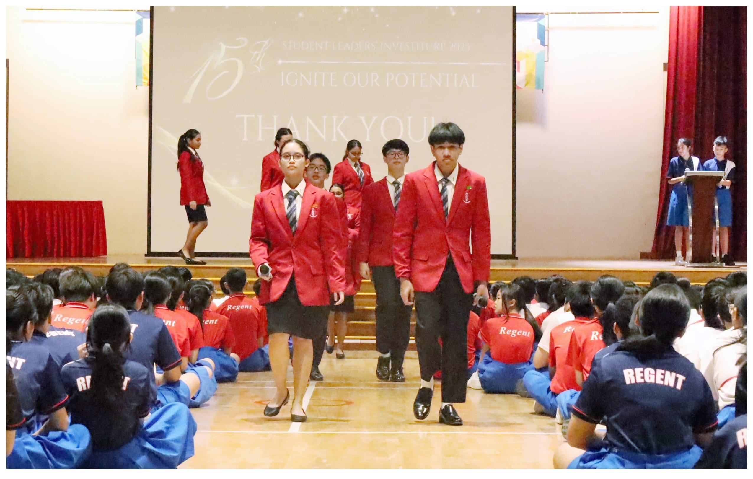 Students in red blazers walk through a seated crowd at Regent school's 15th Student Leaders Investiture ceremony.